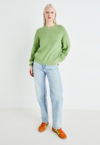 Lys grøn ribbestrikket genser med fallende skuldre, kombinert med lyseblå rette jeans og oransje joggesko med grønne detaljer.