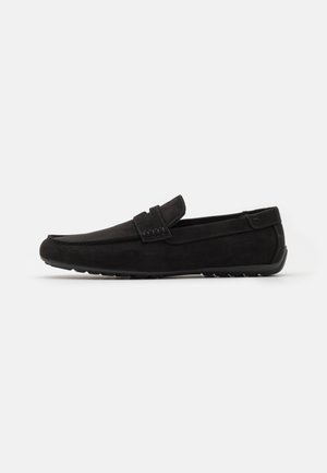 Schwarzer Herren-Loafer aus Wildleder mit Gummisohle und dekorativem Riemen, seitlich auf weißem Hintergrund dargestellt.