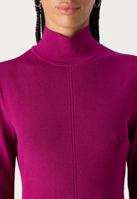 Magenta hochgeschlossenes Oberteil aus geripptem Strickmaterial mit einer zentralen Nahtdetails und figurbetontem Schnitt. Glatte Textur mit langen Ärmeln.