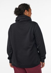 Mustap fleece-huppari, jossa on korkea taitettu kaulus ja ribbaatut hihansuut, rento istuvuus ja sileä pinta, näkyy takaapäin.