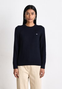 Maglione a maglia blu navy con scollo rotondo, polsini e orlo ribattuti, caratterizzato da un piccolo logo ricamato sul petto.