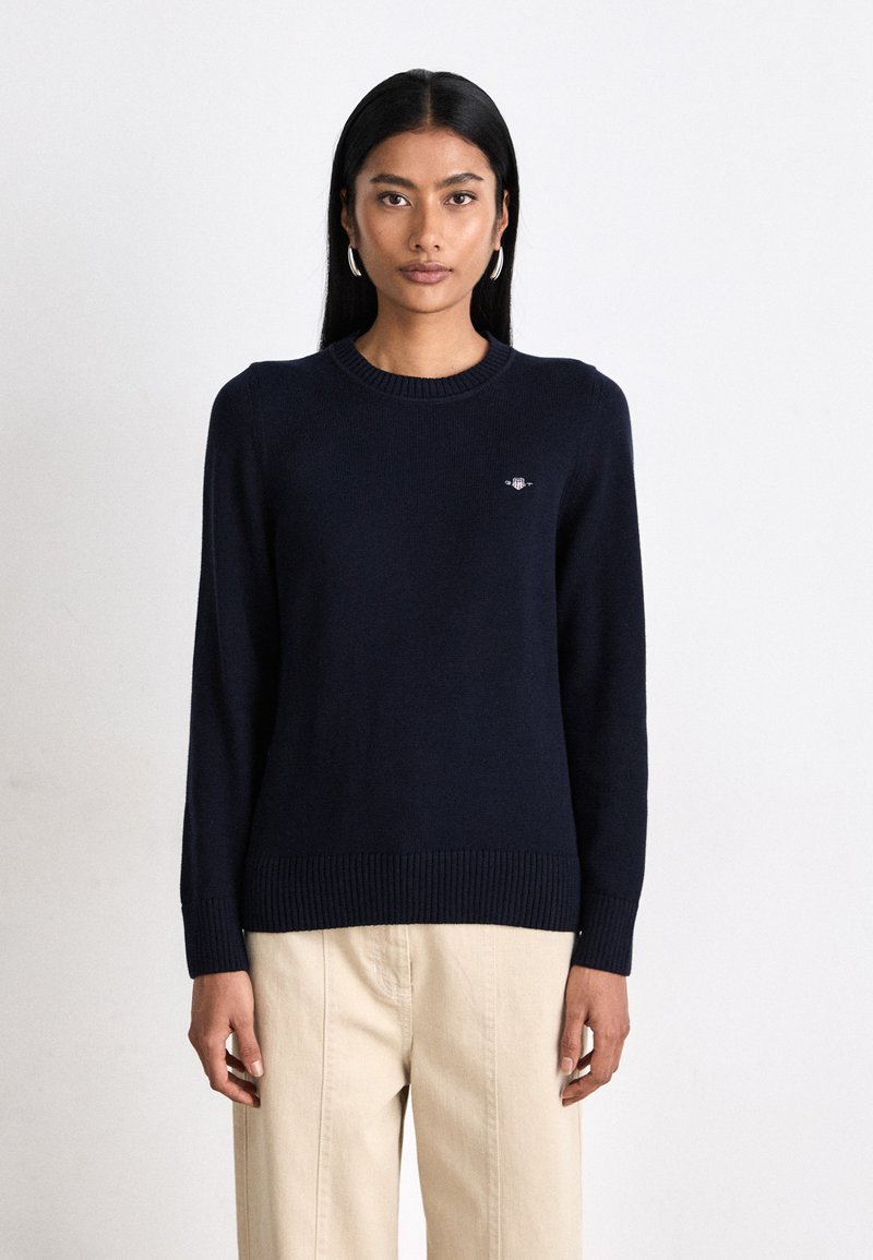 Maglione a maglia blu navy con scollo rotondo, polsini e orlo ribattuti, caratterizzato da un piccolo logo ricamato sul petto.