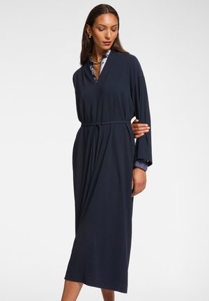 Abito blu navy a maniche lunghe con scollatura a V e vita legata. Tessuto morbido che scende fino a metà polpaccio, con polsini a camicia in contrasto per un tocco di dettaglio.