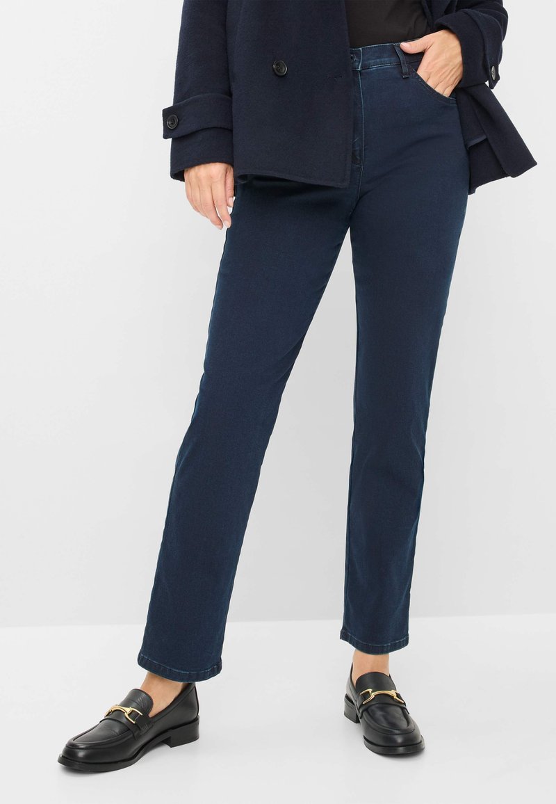 Donkerblauwe denim jeans met een rechte pijp, vijf zakken ontwerp en een klassieke tailleband. Gecombineerd met zwarte instappers met gouden accenten.