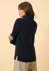 Navyblauer Pullover mit hohem, gefaltetem Kragen, langen Ärmeln und seitlichen Schlitzen, aus einem weichen, strukturierten Material.