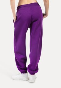 Fialové tepláky s pružným pasem, elastickými manžetami a bočními kapsami, doplněné bílými sportovními botami, vykazující uvolněný střih.