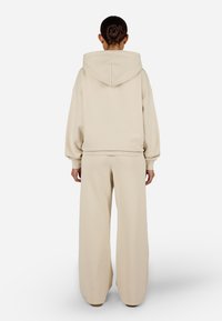Μπεζ ιδανικό για χαλάρωση φούτερ με κουκούλα και παντελόνι φαρδύ, διαθέτοντας ραντισμένα μανίκια και μαλακό, υφασμάτινο κόνισμα, προβαλλόμενο από πίσω.