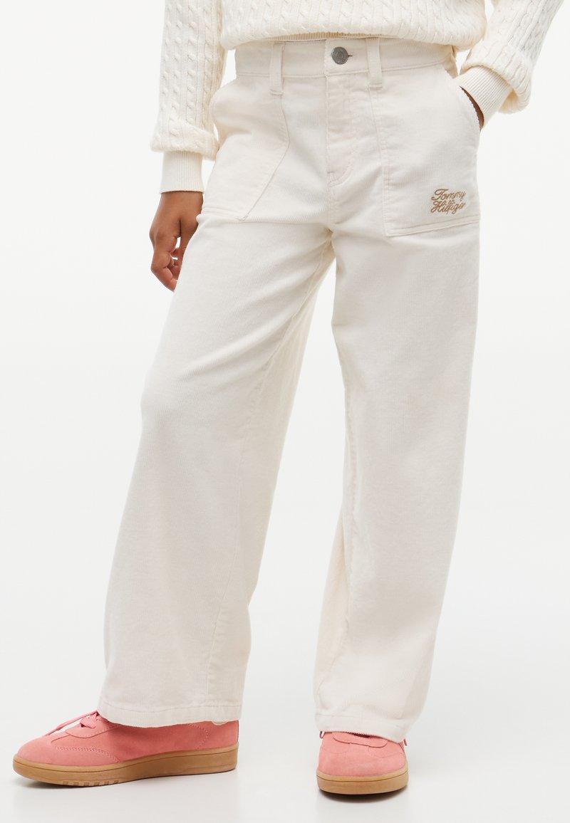Personne portant un pantalon crème à jambes larges avec poches avant et un pull, associé à des baskets roses en daim avec semelles en gomme.