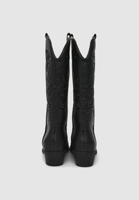 Para czarnych skórzanych kowbojskich butów z haftowanymi wzorami dekoracyjnymi, widocznych od tyłu na neutralnym tle.