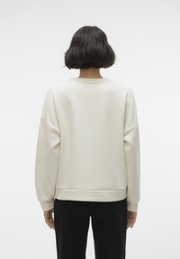 Cream-colored sweatshirt with a relaxed fit, dropped shoulders, and ribbed cuffs, shown from the back. Smooth texture and minimal design.