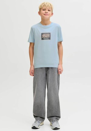 Lichtblauw katoenen T-shirt met een vierkant logo met "JACK & JONES" in wit en oranje. Gecombineerd met grijze jeans met wijde pijpen en sneakers.