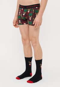 Boxers rouges et verts à motifs de rennes, chaussettes noires avec des accents rouges et un motif de rennes, le tout fabriqué en tissu doux et extensible.