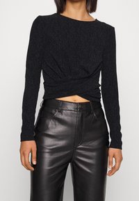 Top nero a maniche lunghe con motivo testurizzato e design attorcigliato sul davanti, abbinato a pantaloni in pelle nera a vita alta.
