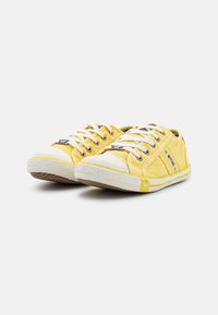 Yellow canvas sneakers with white rubber toe caps and soles. Feature white laces and side accents. Textured fabric with a casual design.