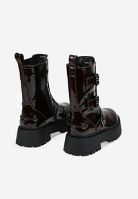 Stivaletti a metà polpaccio in un lucido borgogna scuro, con suole nere spesse, cerniere laterali e tre cinturini regolabili con fibbie sui lati esterni.
