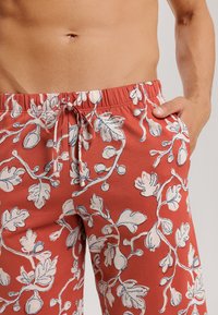 Rote Badeshorts mit einem weißen Blumenmuster; elastischer Bund mit Kordelzug; seitliche Taschen; leichter Stoff mit glatter Textur.
