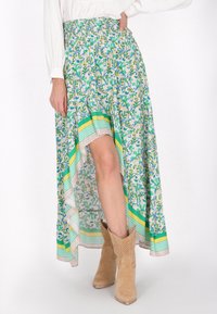 Gonna fluida in tessuto leggero con motivo floreale verde e giallo, orlo asimmetrico e bordo decorativo a righe nella parte inferiore.