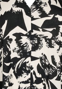 Svart och vit blus med ett abstrakt mönster, i ett texturerat tyg och med fem knappar fram. Mönstret innehåller djärva penseldrag.