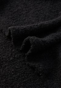 Tissu noir texturé avec une surface douce et duveteuse, présentant des bords enroulés et une apparence froissée, mettant en avant sa texture épaisse et moelleuse.