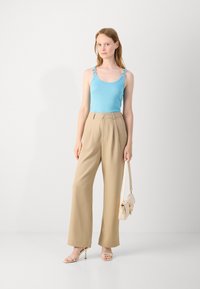 Light blue tank top with decorative straps, beige high-waisted pants, beige handbag, and nude strappy heels against a plain background.