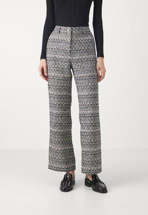 Vevde brede bukser i svart, hvit og grå, med et teksturert mønster og høyt liv, sammen med svarte loafers.