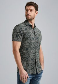 Korte mouw shirt in donkergroen met een contrasterend palmenbladenpatroon. Voorzien van een knoopsluiting aan de voorkant en een klein embleem op de borst.