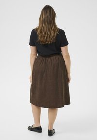 Brown corduroy skirt with an elastic waistband, knee-length, and a smooth texture. Paired with a black short-sleeve top and black shoes.