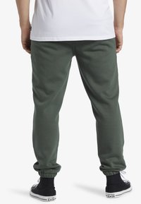 Groene joggers van zachte stof, met een ontwerp van omgeslagen enkels. Gepaard met zwarte high-top sneakers met witte accenten.