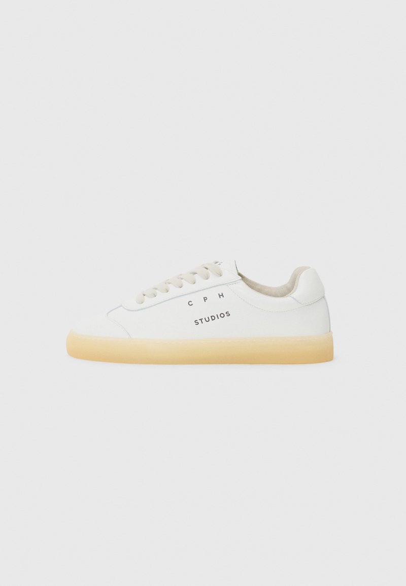 White sneakers made of leather with a round toe, beige laces, and a translucent gum sole; features "CPH STUDIOS" logo on the side.