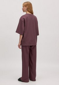 Overmaat, t-shirt met korte mouwen en wijde broek in een gedempte paarse stof. Heeft een ronde halslijn en een ontspannen pasvorm. Soepele textuur.