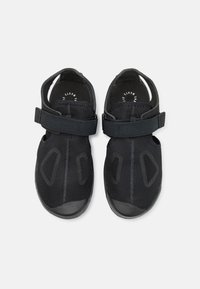 Czarne buty sportowe z siateczkową cholewką, regulowanymi paskami i gumowymi podeszwami. Posiadają wycięcia oraz wzmocniony obszar palców.