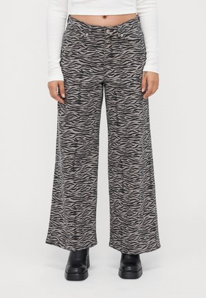 Woman wearing wide-leg pants with gray and black zebra print, white long-sleeve cropped top, and black platform ankle boots.