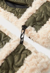 Gequilte groene stof met een zachte beige afwerking, voorzien van een zwart cliphardwaredetail. Zachte textuur met contrasterende kleuren.