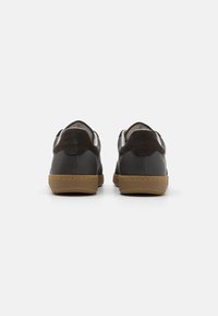 Sneakers de couro preto com solas de borracha castanha. Apresentam uma textura suave, colarinho almofadado e biqueira contrastante. Design minimalista.