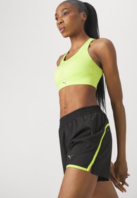 Sujetador deportivo verde neón con una textura suave y detalles perforados, combinado con pantalones cortos negros que cuentan con acentos neón y una cintura elástica.