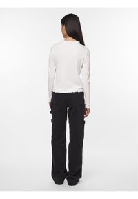 Vit långärmad ribbad topp med vågig halsringning, parat med högmidjade svarta cargobyxor med sidofickor och avslappnad passform.