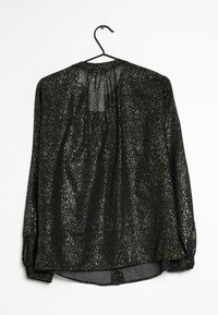 Blusa nera a maniche lunghe con un motivo lucido a macchie. Presenta un retro arricciato e un orlo arrotondato. Il materiale appare leggero e semi-trasparente.