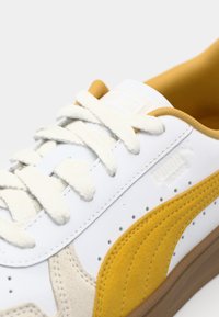 Hvit lær sneakers med gule semsket detaljer, teksturert beige panel, bomullslisser og gummisåle. Logo preget på tungen.