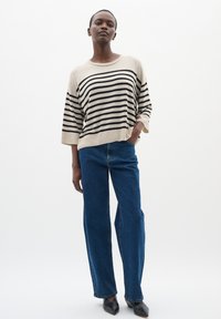 Maglione oversize a righe beige e nere con maniche ampia, abbinato a jeans blu a vita alta e scarpe nere a punta.