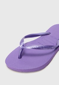 Violet spalvų flip-flop sandalai su tekstūruotu guminiais padu ir blizgiomis dirželiais su logotipu, skirti kasdieniam nešiojimui.