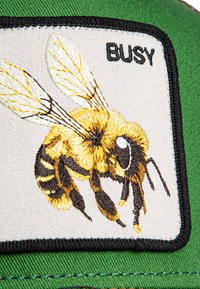 Patch brodé représentant une abeille jaune et noire sur un fond clair, avec le mot "BUSY" en noir, sur une casquette verte.