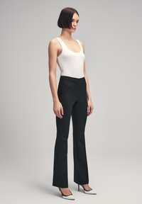 Zwarte flared broeken met een smooth textuur, met een slim fit bij de heupen en een hoge taille. Gecombineerd met een witte geribbelde tanktop.