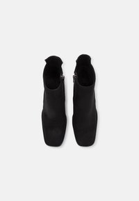 Bottines en daim noir, à bout carré, dotées de fermetures éclair sur les côtés et d'une texture lisse, conçues avec des accents minimalistes.