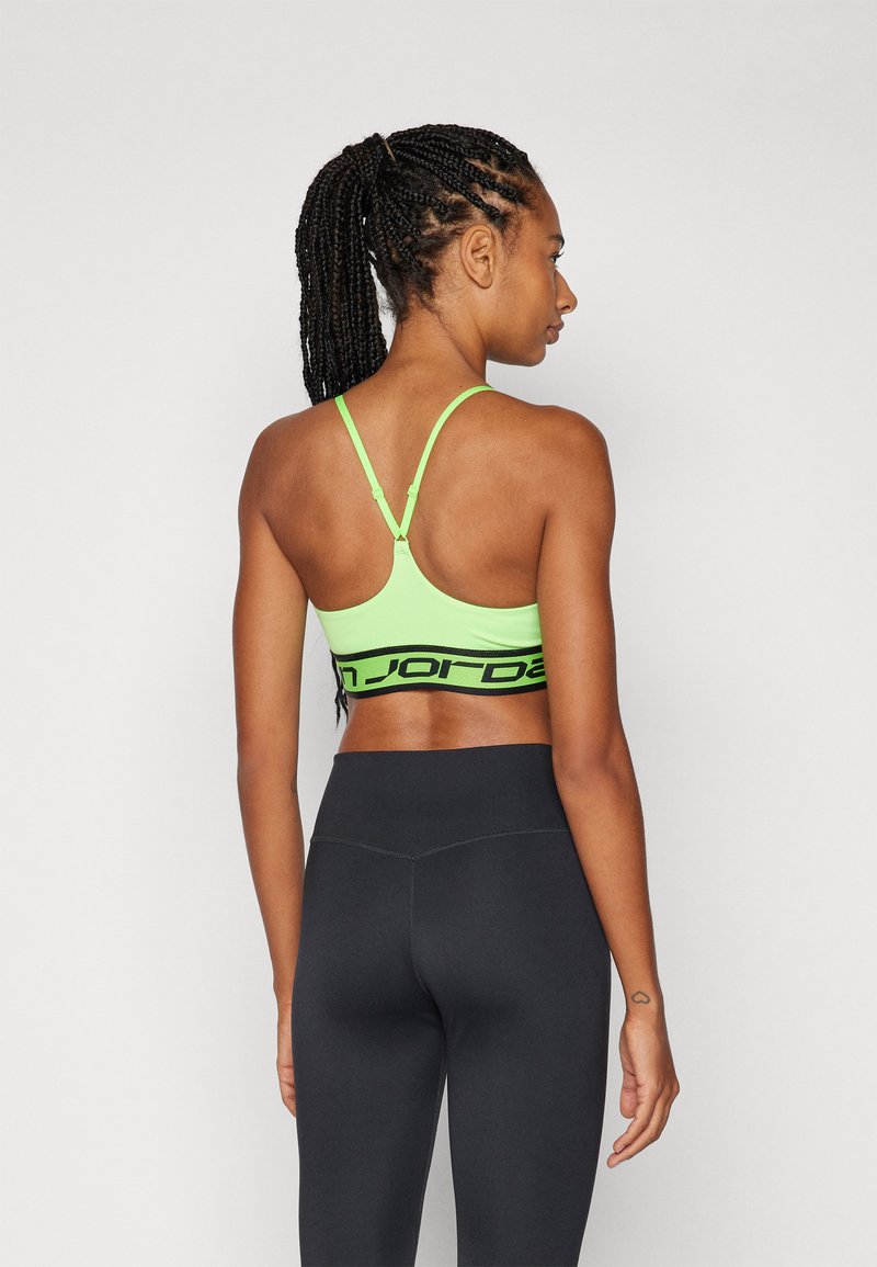 Sujetador deportivo verde con una banda de logo negro, con tirantes finos ajustables y un diseño de espalda cruzada. Combinado con leggings negros de talle alto.
