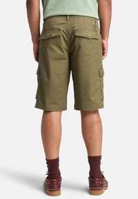 Pantaloncini cargo verde oliva con multiple tasche, vestibilità comoda e cuciture in vista, abbinati a calze bordeaux e scarpe marroni.