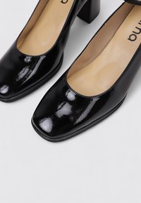 Escarpins en cuir verni noir avec un bout carré et une finition lisse. Dotés d'un talon épais pour plus de stabilité.