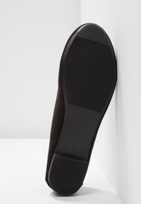 Semelle de chaussure en daim noir avec grip en caoutchouc texturé, bout arrondi, et un indicateur de taille "37" sur le talon. Design plutôt plat, esthétique minimaliste.