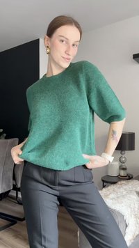 Green wool blend short-sleeve sweater with loose fit, worn over black tailored pants. Smooth texture, slightly oversized design.