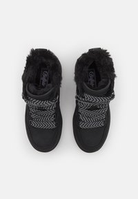 Bottes d'hiver noires avec des lacets épais à motif noir et blanc et une doublure en fourrure moelleuse autour de la cheville.