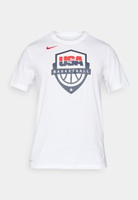 Bílá bavlněná tričko s krátkým rukávem. Uprostřed se nachází velké logo USA Basketball v modré, červené a černé barvě.